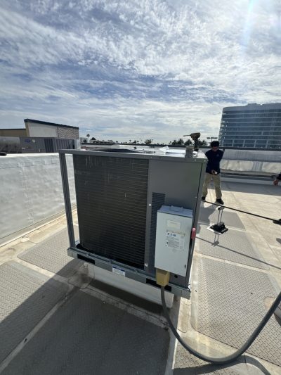 A large HVAC unit is installed on a rooftop under a partly cloudy sky, with a person standing near the edge of the roof in the background.