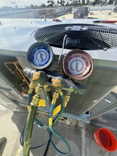 Close-up of HVAC manifold gauges connected to an outdoor air conditioning unit on a rooftop during maintenance.