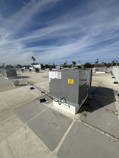 Large HVAC unit installed on a flat rooftop under a partly cloudy sky, surrounded by additional HVAC units and rooftop fixtures.