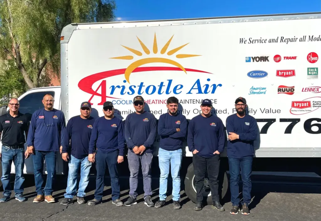 Seven men stand in front of an Aristotle Air service truck, all wearing matching shirts with the company logo. The truck displays HVAC brand logos and company information.